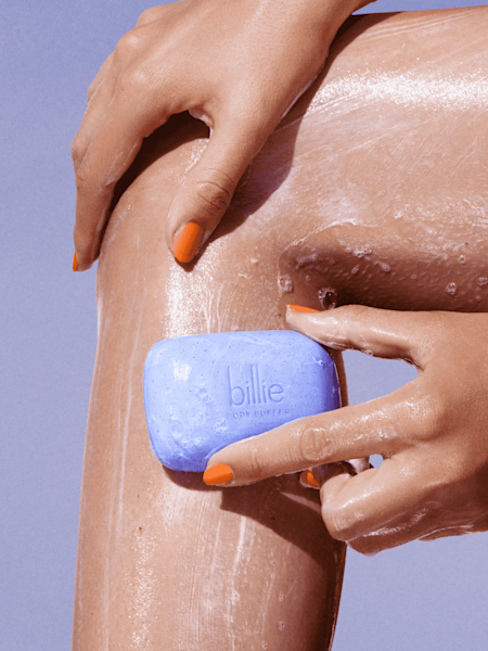 model holding purple body buffer exfoliating bar against her leg